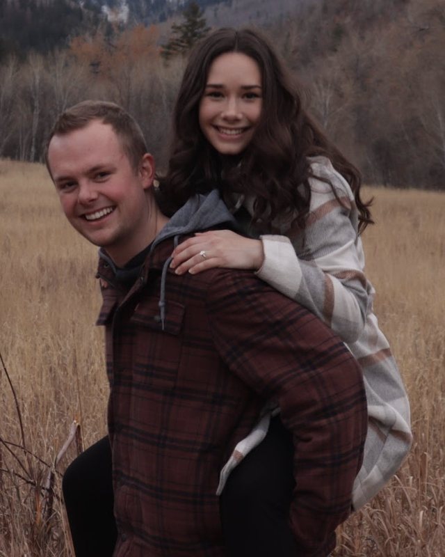 Cameron and Alia Woolstenhulme, smiling in a grassy mountain meadow, Alia riding on Cameron's back
